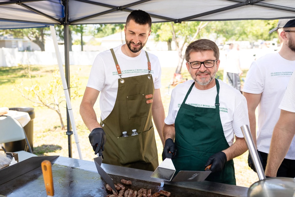 Two volunteers in aprons grilling food outdoors